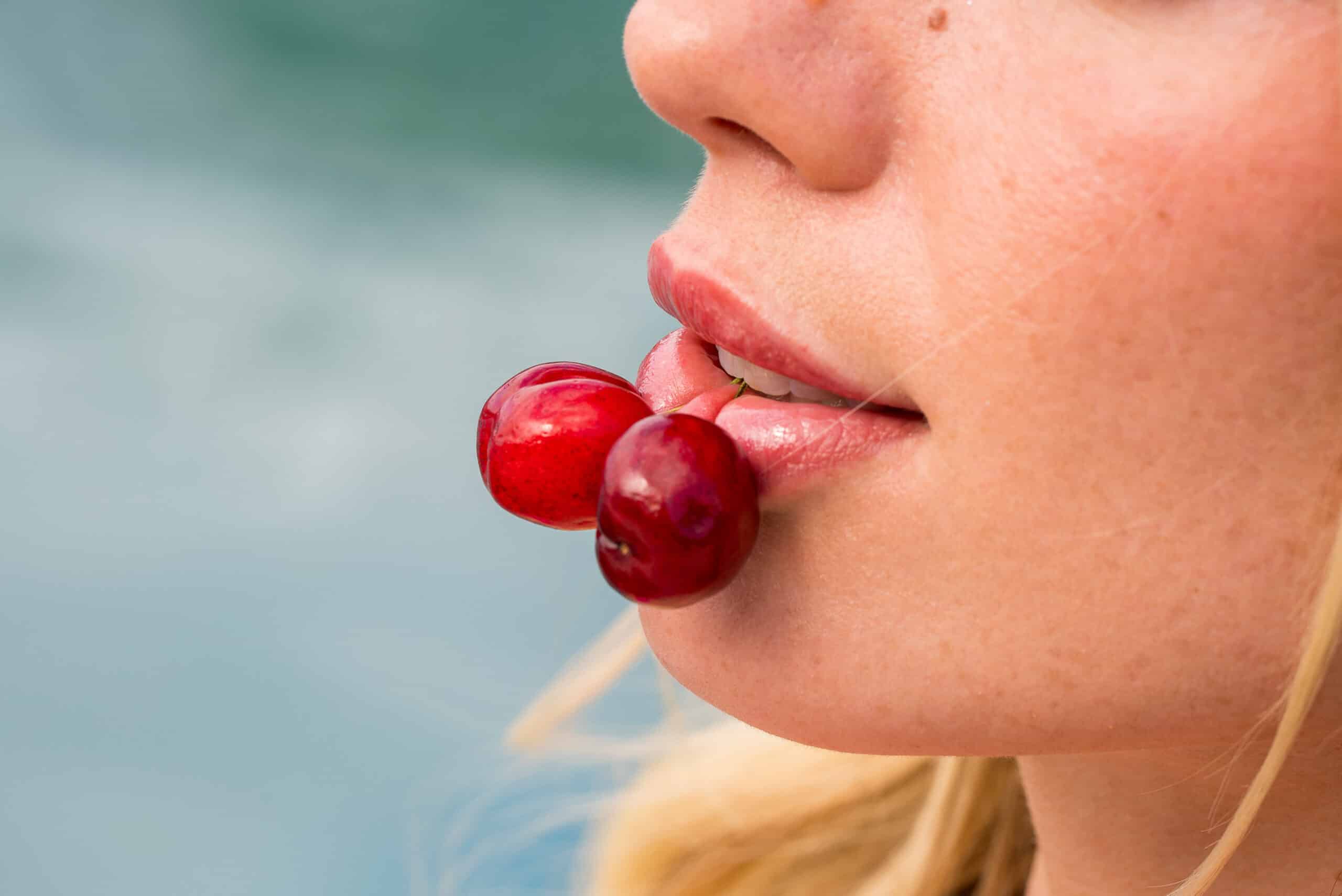 Close-up of a woman with cherries in mouth.